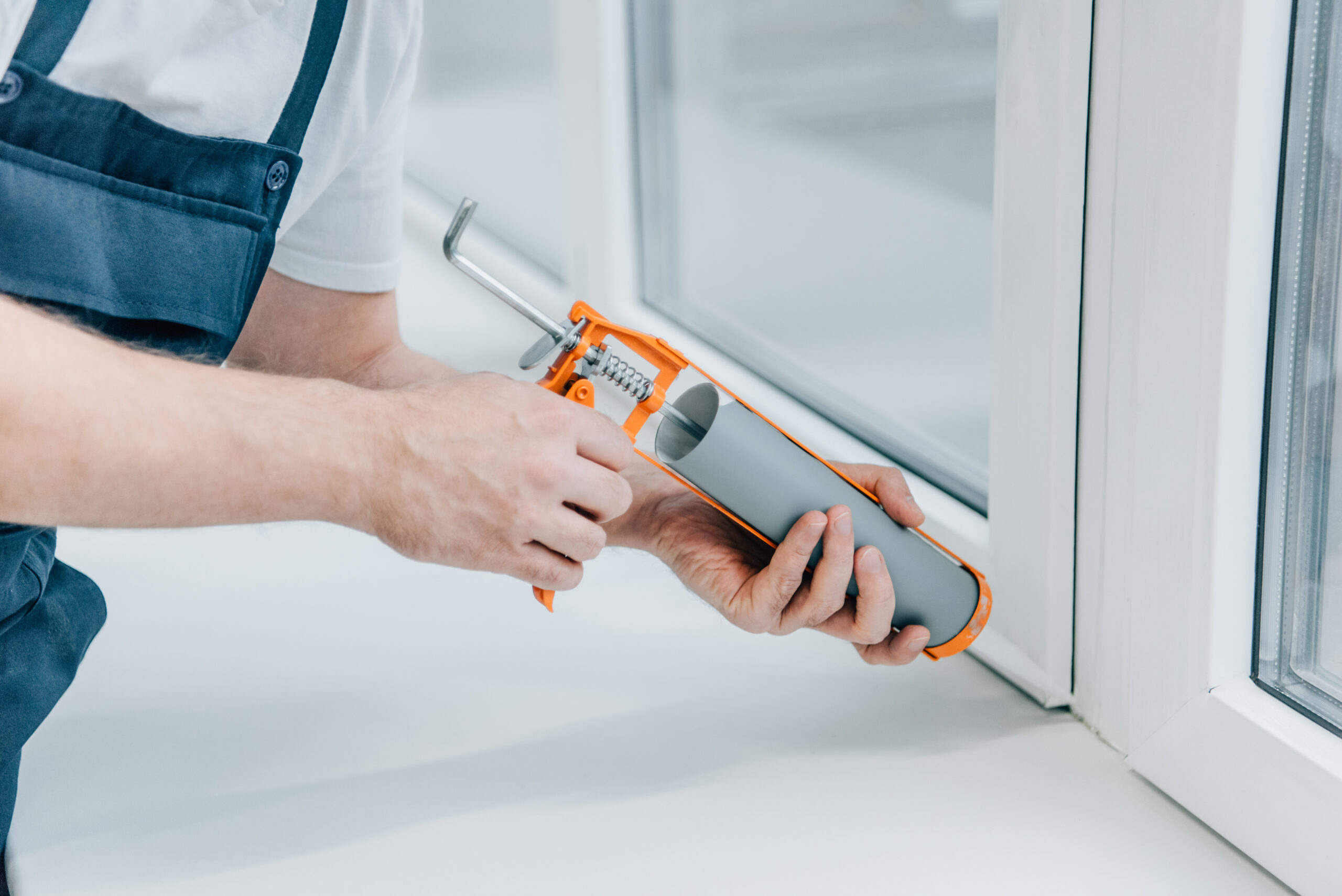 cropped image of male repairman fixing window with sealant gun